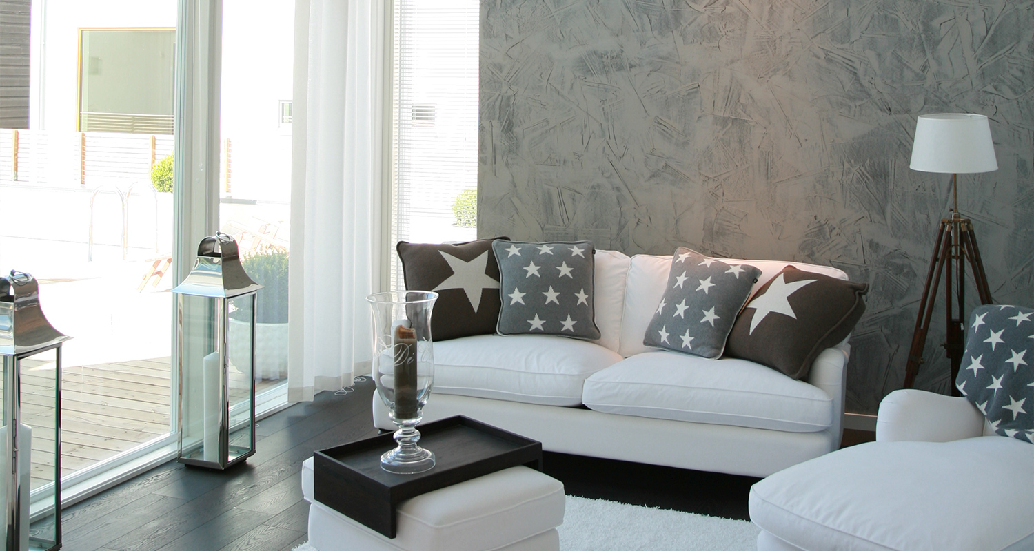 Moderni olohuone, valkoinen kulmasohva harmailla tähtityynyillä, tumma puulattia, betoniseinä