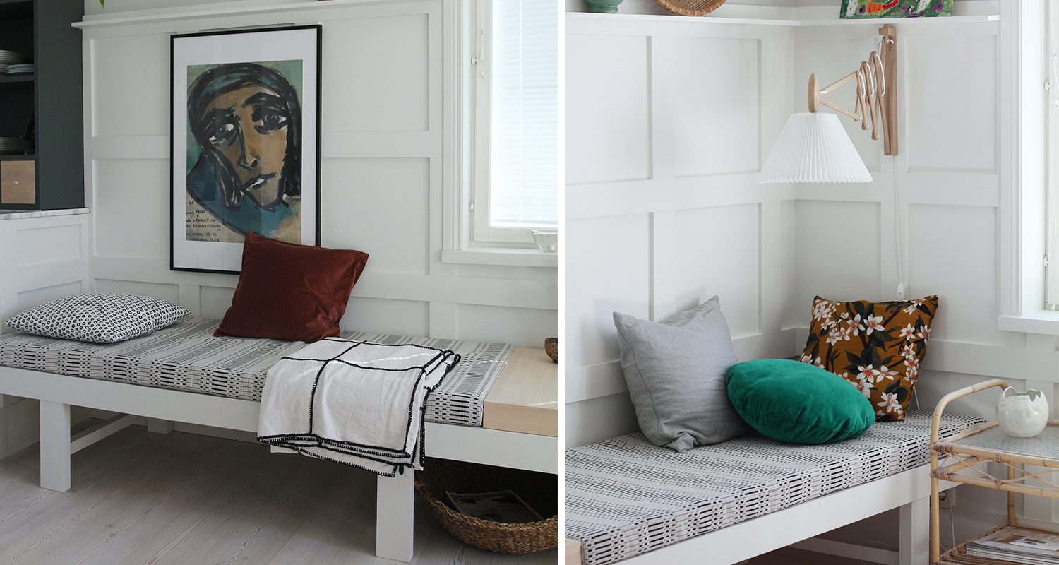 Valkoinen penkki paneeliseinän edessä, harmaa kuviopatja, vihreä ja kukkainen tyyny.