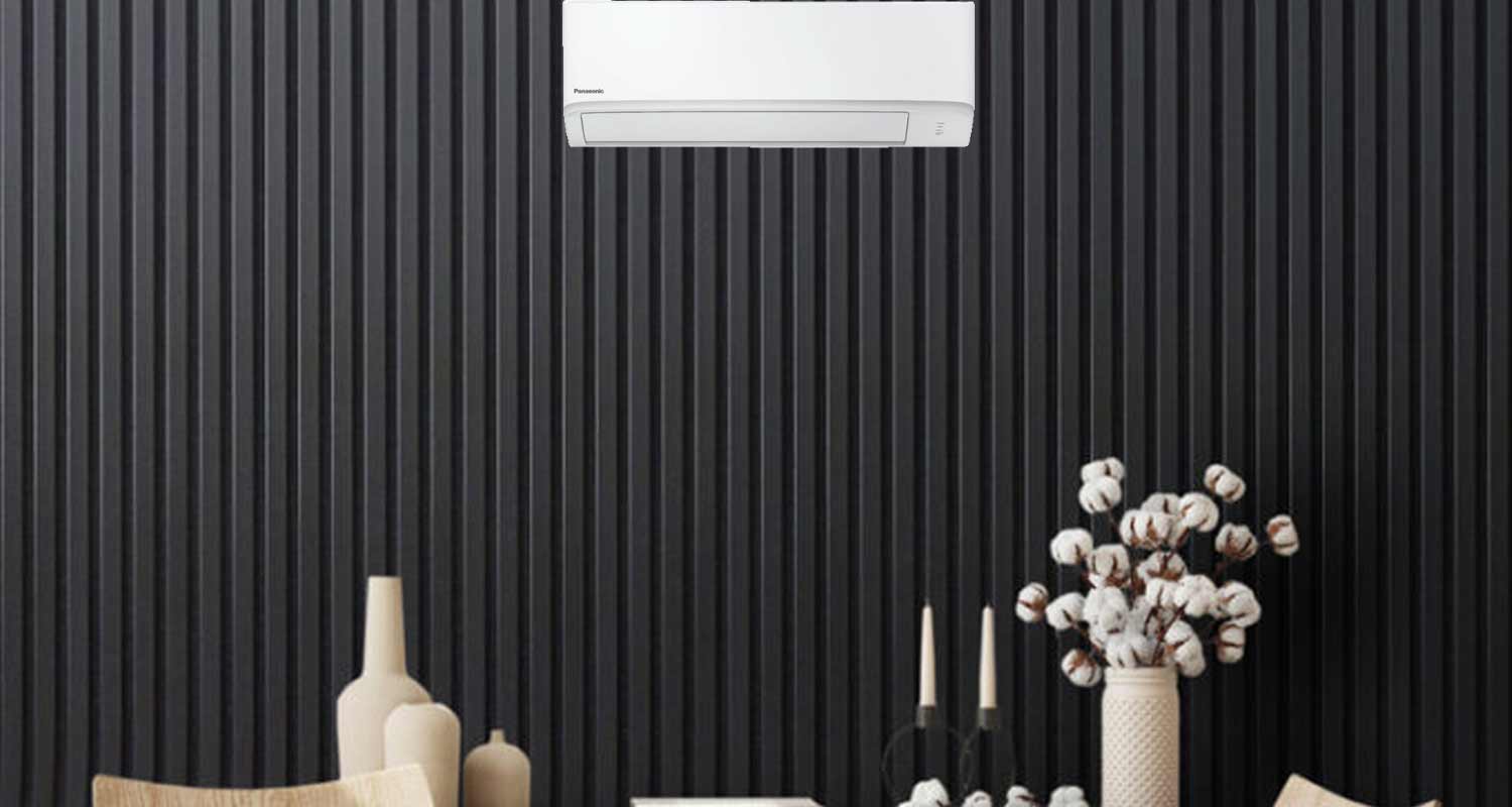 Valkoinen Panasonic-ilmastointilaite mustalla lautaseinällä, beigejä vasuja ja pumpulioksia