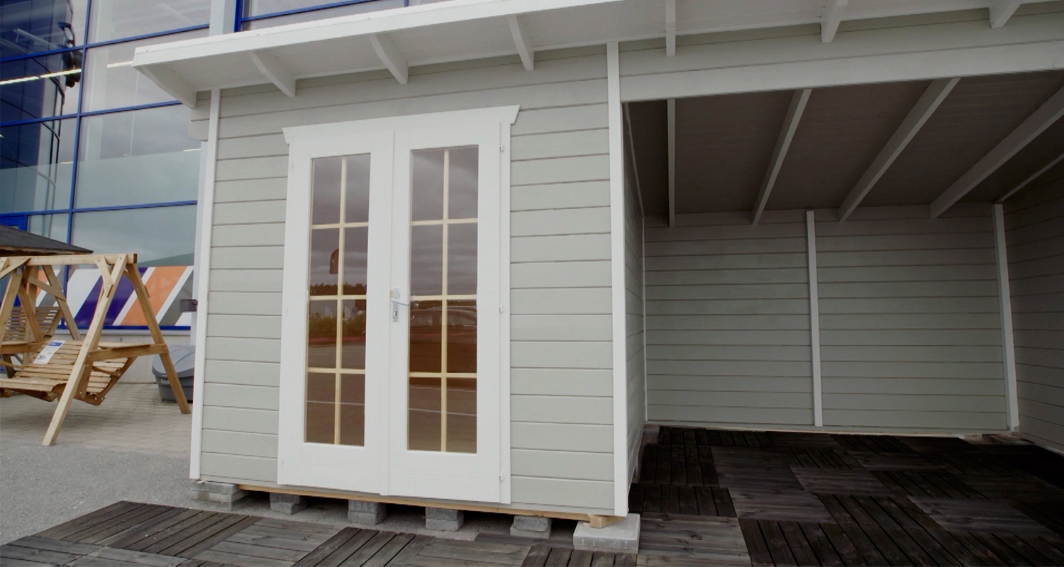 Vaaleanharmaa pihavarasto valkoisilla lasiovilla, tumma puulattia kaupan edustalla