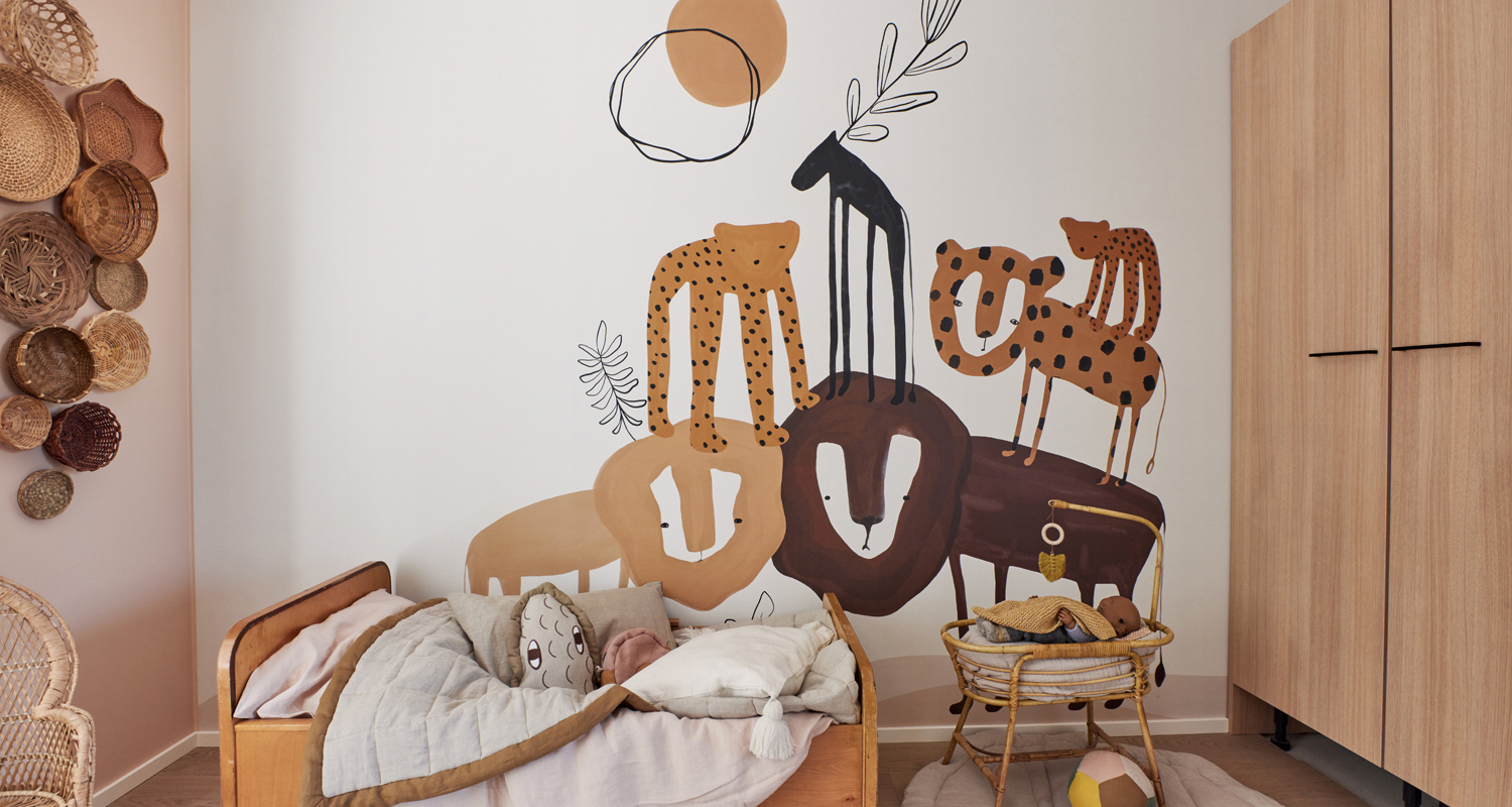 Pastellinsävyinen lastenhuone: ruskeasävyinen savannieläinmuraali, puusänky ja seinäkoreja.