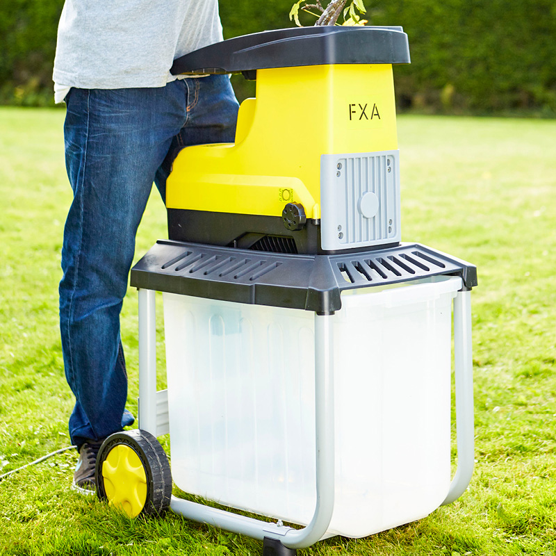 Ihminen työntää oksia keltamustaan puutarhakutteriin nurmikolla.