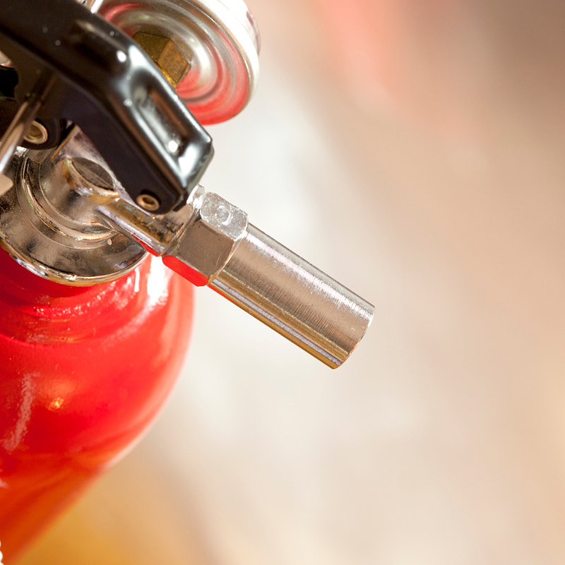 Punaisen palosammuttimen metallinen suutin ja musta kahva lähikuvassa.