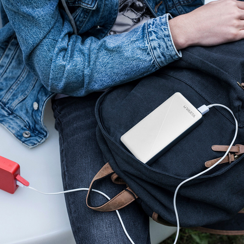 Sinisessä farkkutakissa mustan repun päällä valkoinen Varta-varavirtalähde ja punainen laturi.