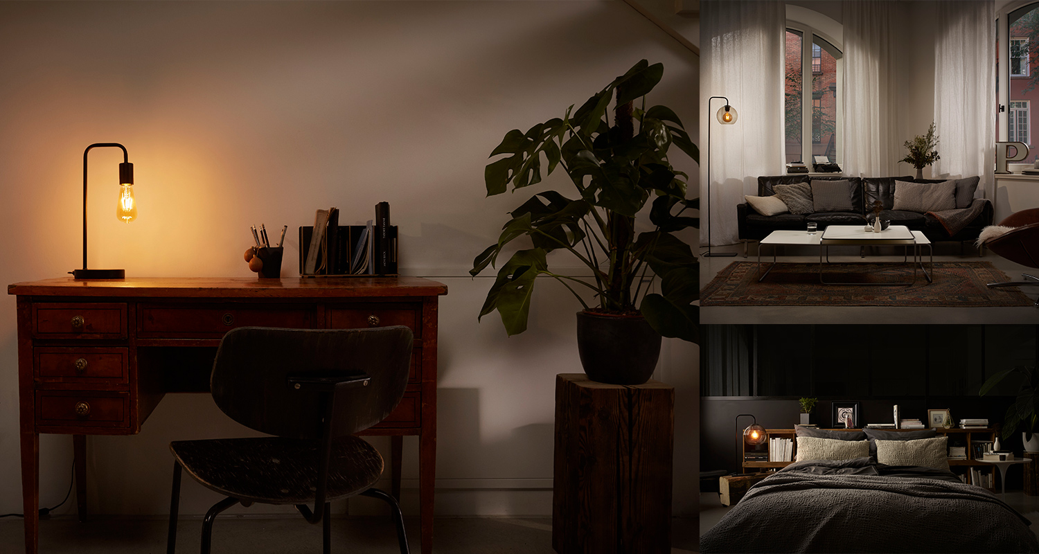 Kolmessa huoneessa: lämmin pöytälamppu puupöydällä, vihreä huonekasvi, musta sohva ja tumma sänky.