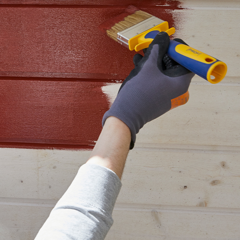 Mies maalaa mökin ulkoseinää punaisella.