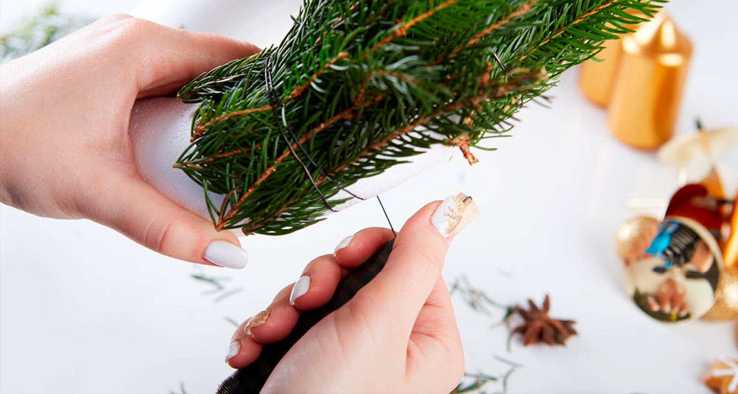 Nainen sitoo joulukranssia. Pöydällä näkyy joulukranssi sekä koristeita.