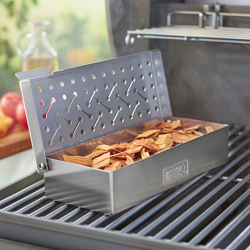 Avonainen ruostumaton savukotelo täynnä vaaleita puulastuja grilliritilällä ulkona