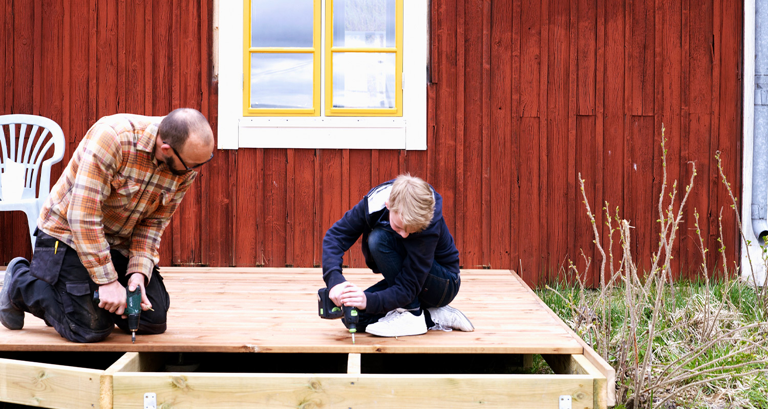 Terassin perustus rakentuu helposti asiantuntijan ohjeilla. Kuvassa mies ja poika tekemässä terassin perustusta.