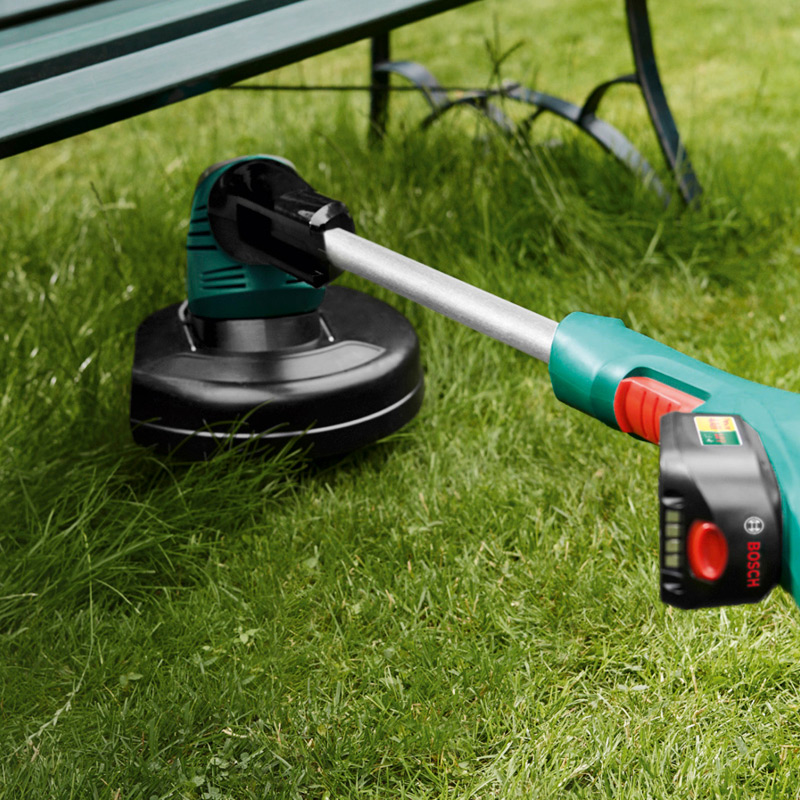 Vihreä-musta Bosch-akkuinen ruohotrimmeri penkin alla vihreällä nurmikolla.