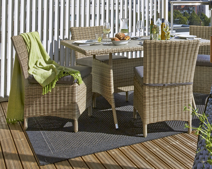 Beigen rottinkiparvekeryhmä: neljä tuolia, pöytä astioineen, leipäkulho ja vihreä huopa.