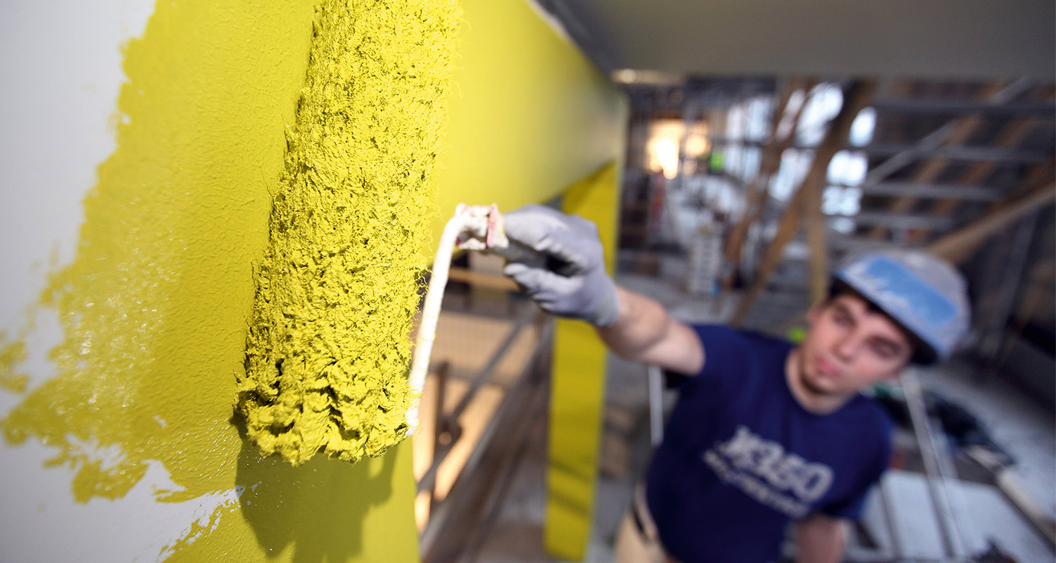Ammattilainen maalaa Tikkurilan Ässä-maalisarjan keltaiseksi sävytetyllä maalilla julkisen tilan seinää