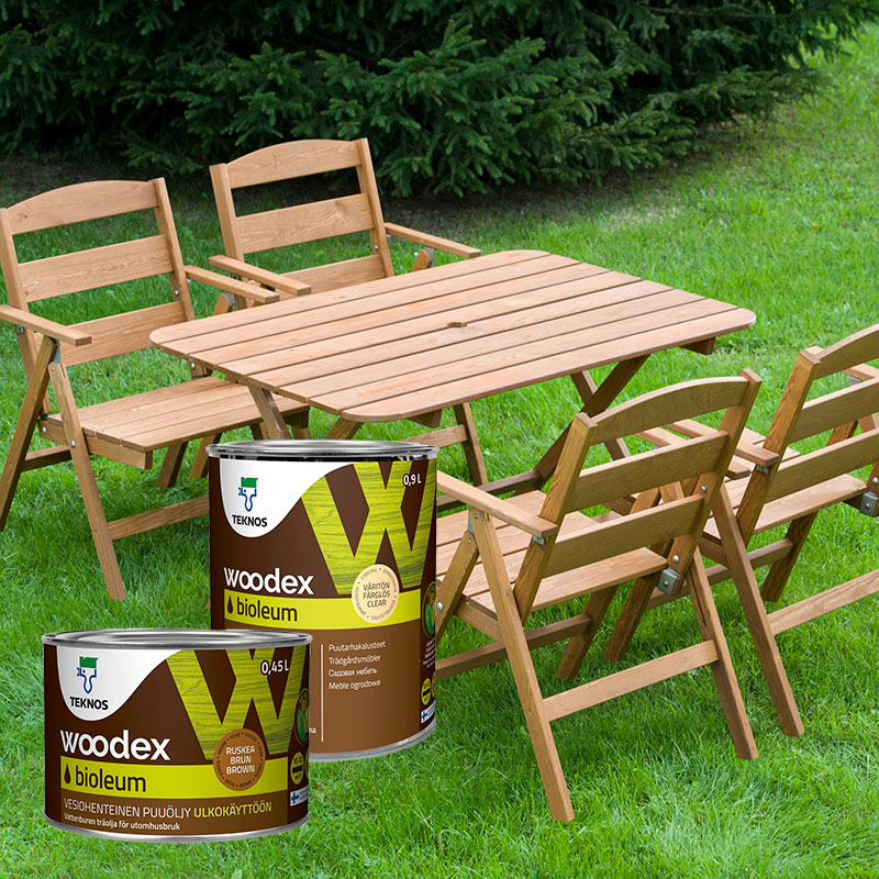 Vihreällä nurmella puinen puutarhapöytä ja tuolit, edessä kaksi ruskeaa Woodex Biooleum -öljyä.