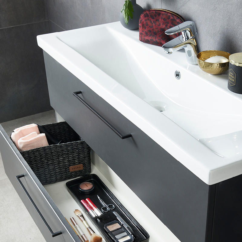 Valkoinen allas tummanharmaassa kaapissa, avoin laatikko pyyhkeitä ja meikkisiveltimiä.