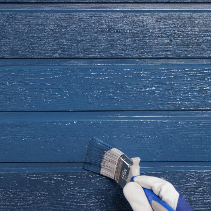 Pensseli valko-sinisessä hansikkaassa maalaa sinisiä vaakasuoria puulautoja