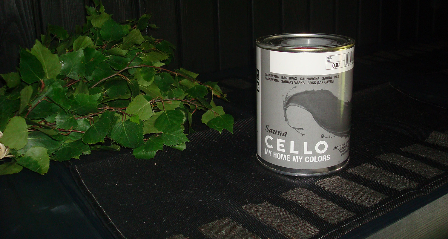 Musta alusta, vihreät koivunoksat vasemmalla ja harmaa Sauna Cello -saunavahapurkki oikealla.