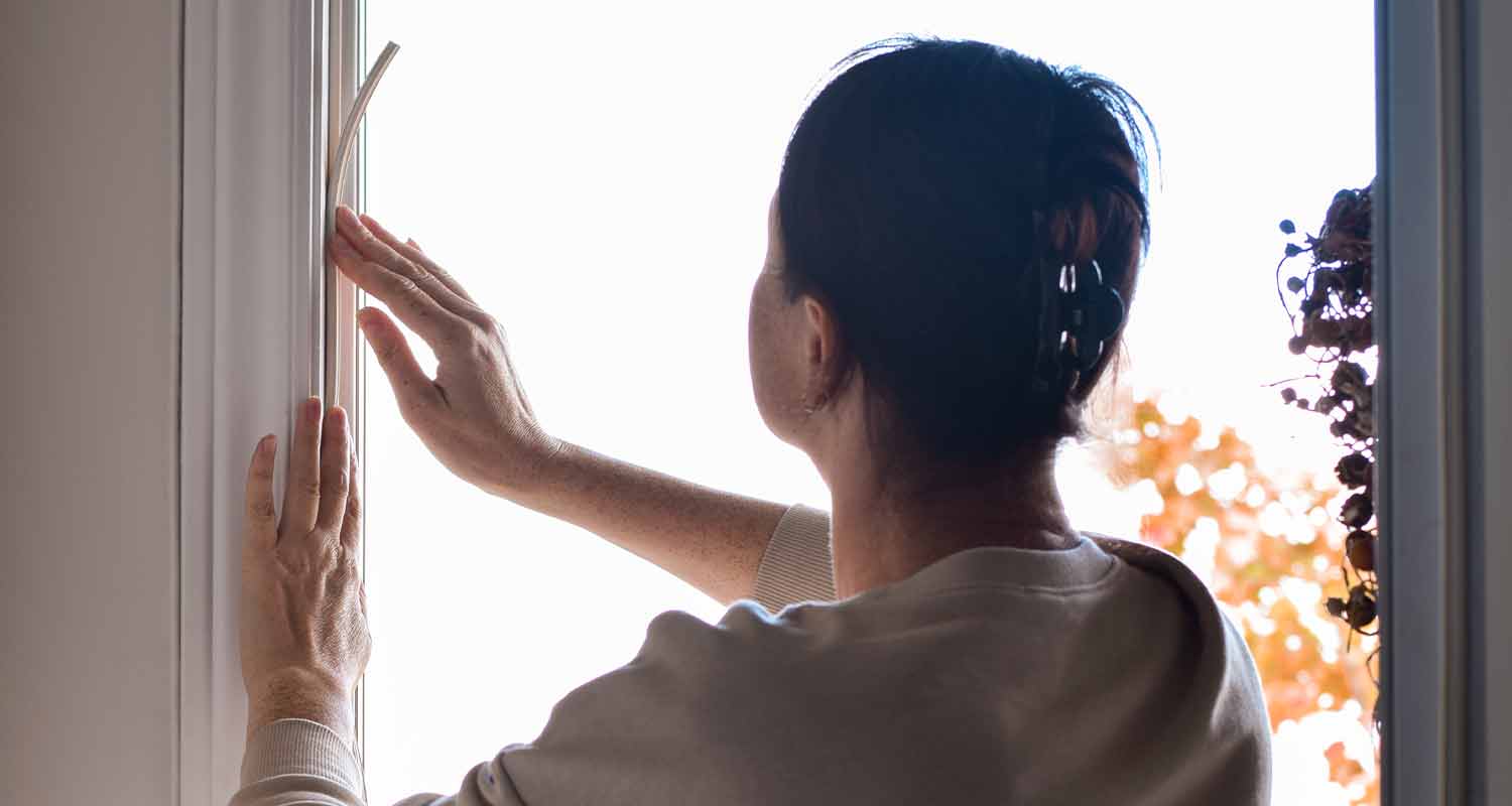 Ruskeahiuksinen nainen avaa valoa tulvivaa ikkunaa, taustalla oransseja syyslehtiä.