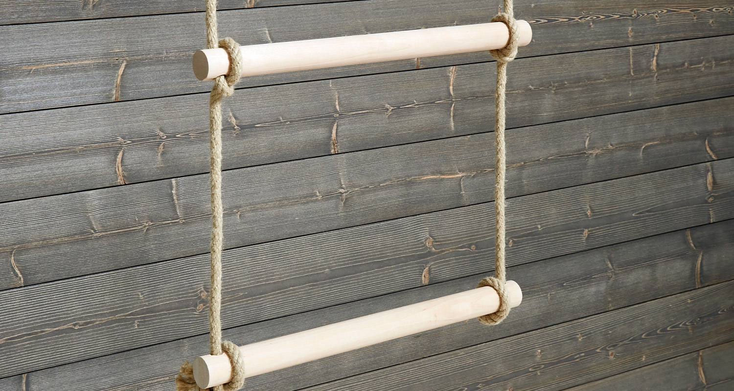 Vaaleat puutangot roikkuvat köysissä harmaan puupaneeliseinän edessä.