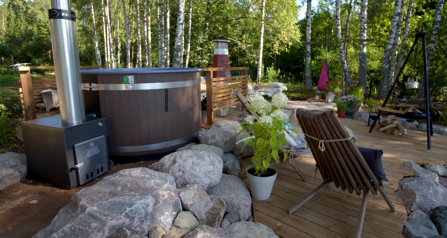 Ruskea puuporeamme metallipiipulla kivillä reunustetulla terassilla koivumetsän laidalla.