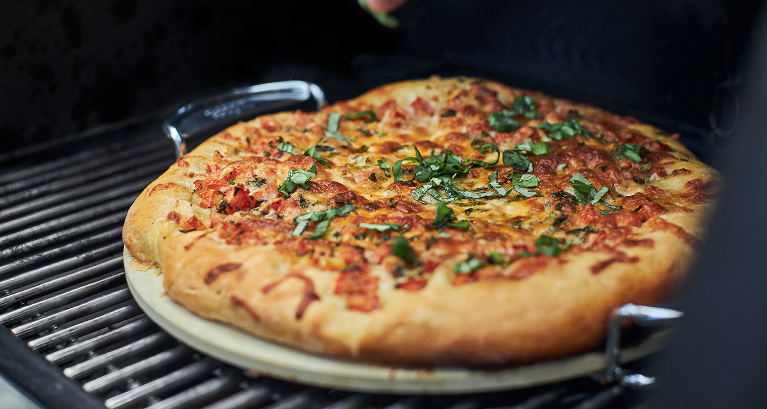 Kullanruskea tomaatti-juustopizza grillissä, päällä tuoretta vihreää basilikaa