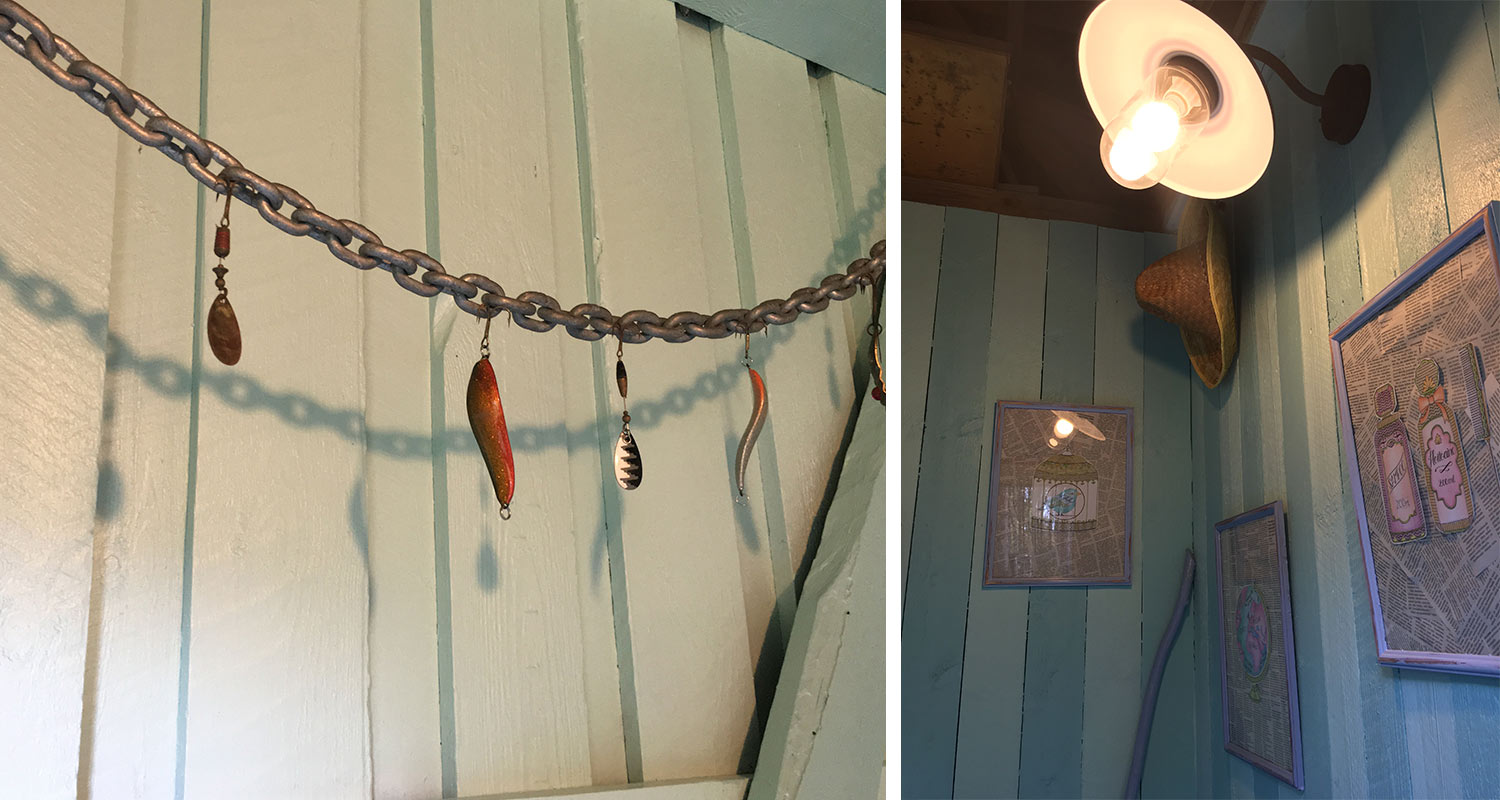 Turkoosi puupaneeliseinä, ketjussa roikkuvat vieheet varjoineen, lamppu, olkihattu ja taulut