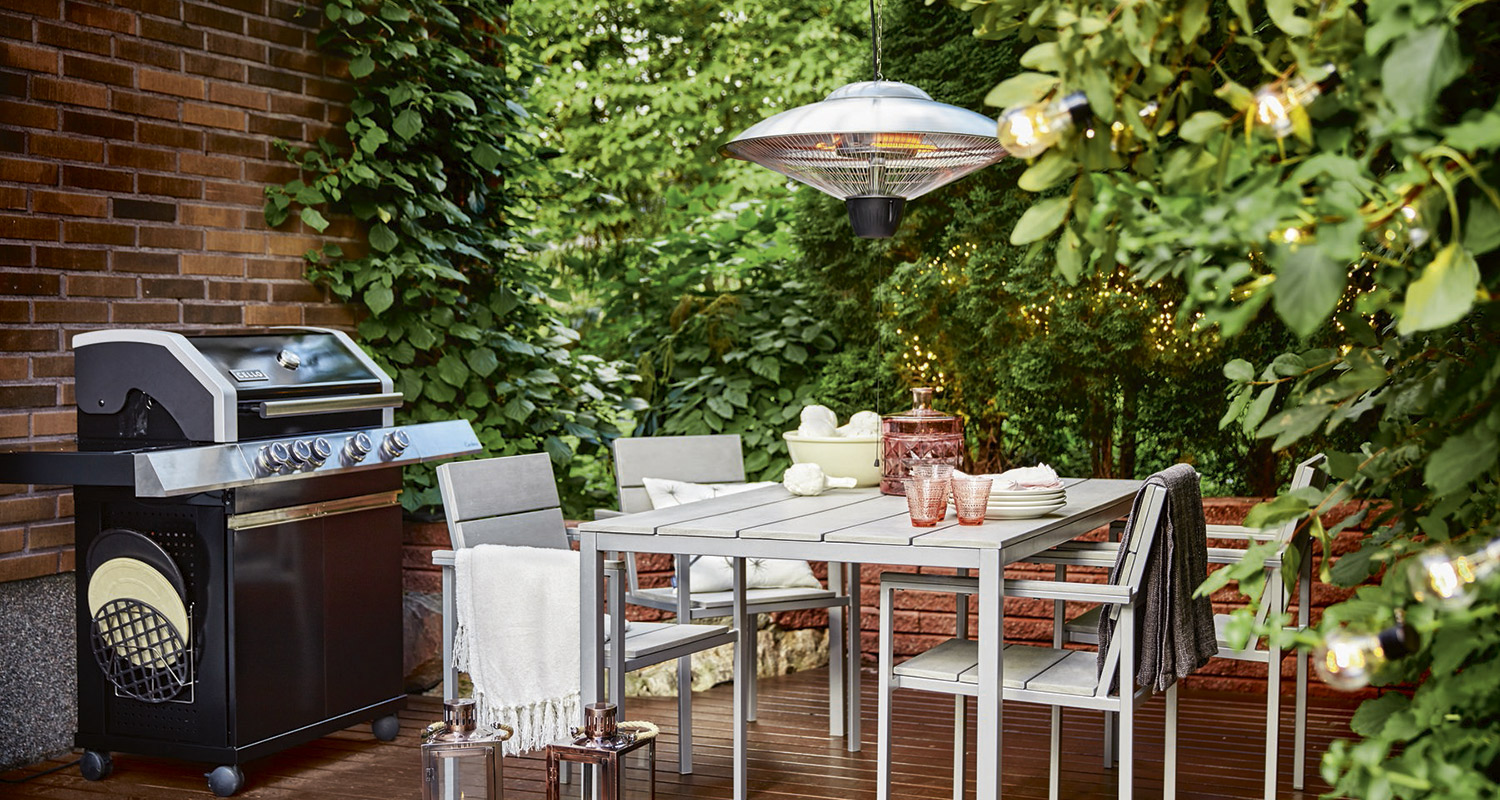 Harmaa terassiryhmä ja grilli vihreiden kasvien, infrapunalämmittimen ja valosarjan ympäröimänä.