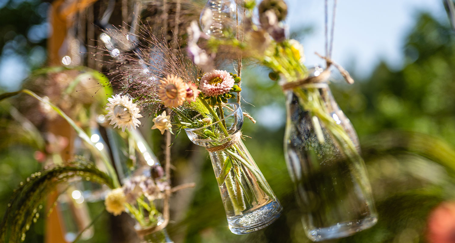 Puutarhapöytä koristetelineellä kesäkeittiön terassilla. Lähikuva leikokukista koristepulloissa.