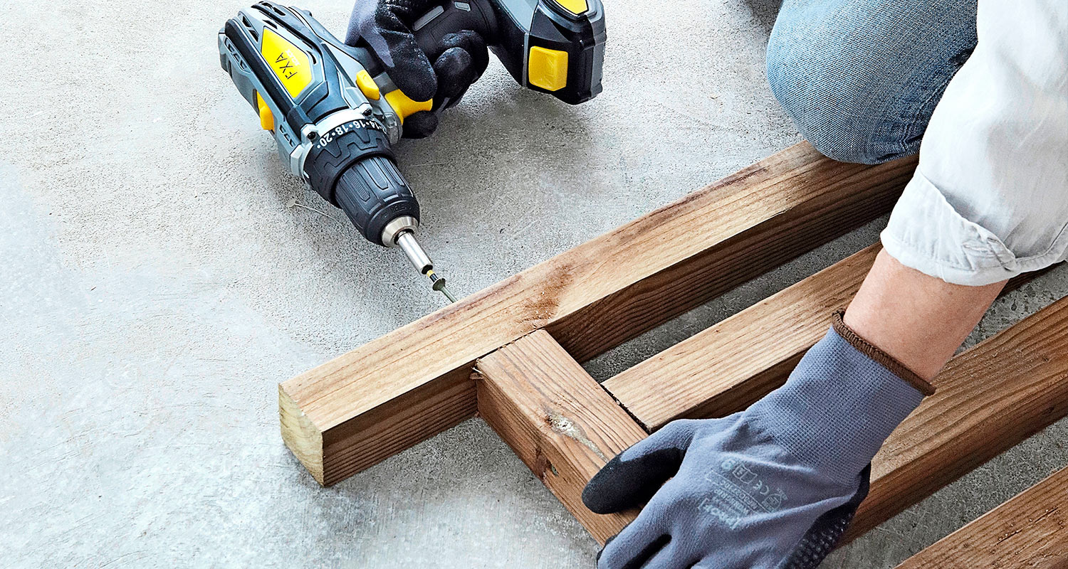 Mies rakentaa sadevesitynnyrin näkösuojaa. Kuvassa ruuvataan sadevesitynnyrin alustan osia yhteen. 