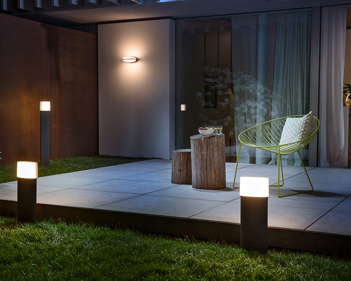 Illan hämärässä valaistu terassi: pilarivalot, vihreä metallituoli ja puupölkky-pöytä