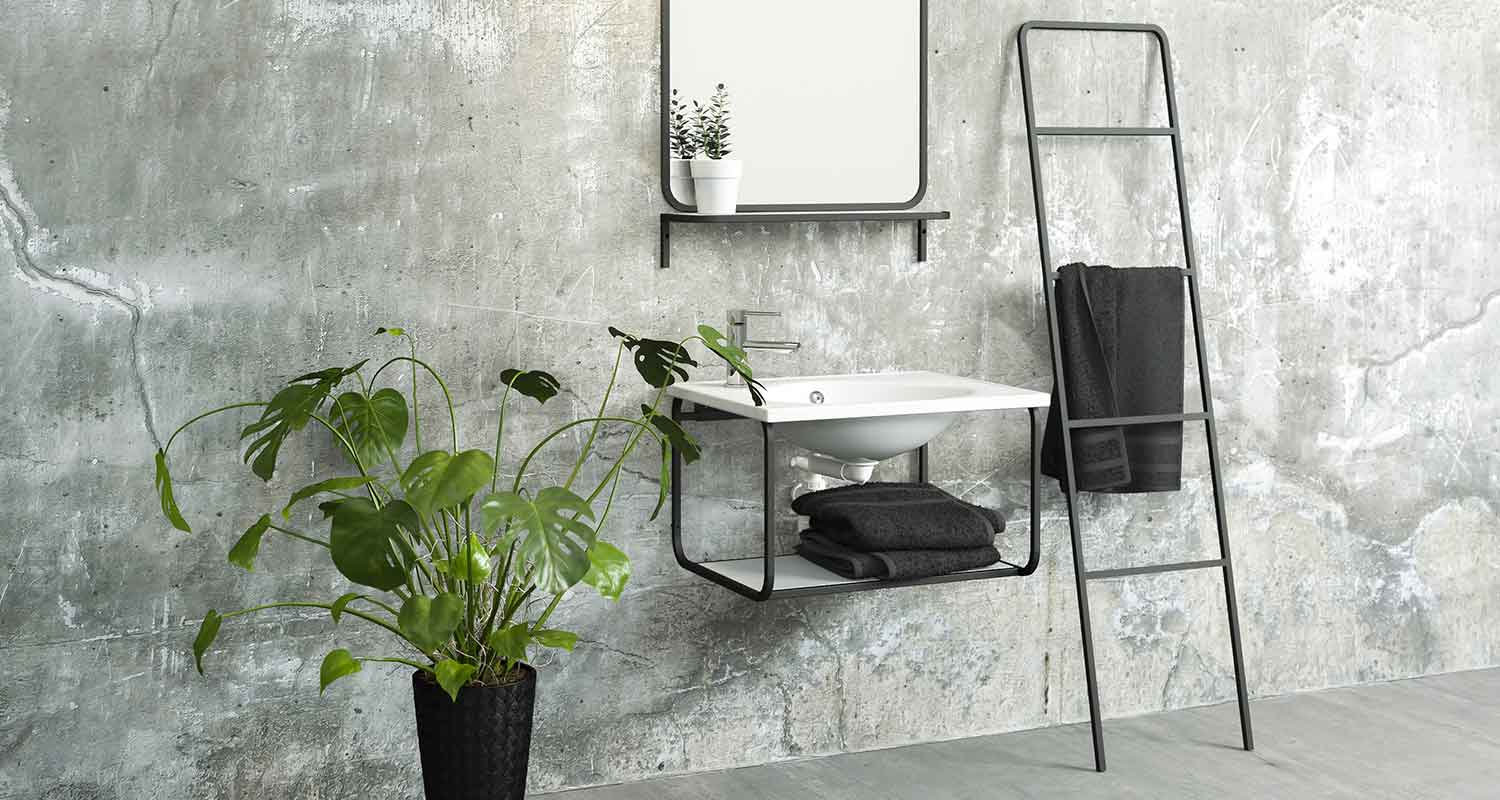 Betoniseinä, valkoinen allas mustassa kehikossa, mustat pyyhkeet telineessä ja vihreä ruukkukasvi.