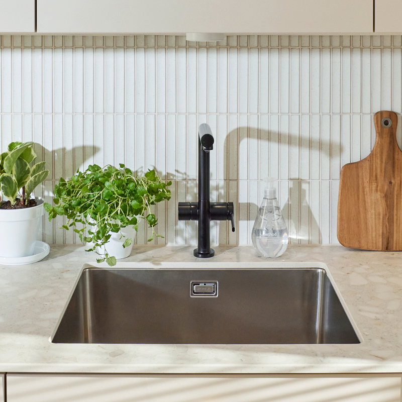 Vaalea keittiö, musta hana keskellä, vasemmalla yrtit, oikealla saippua ja leikkuulauta