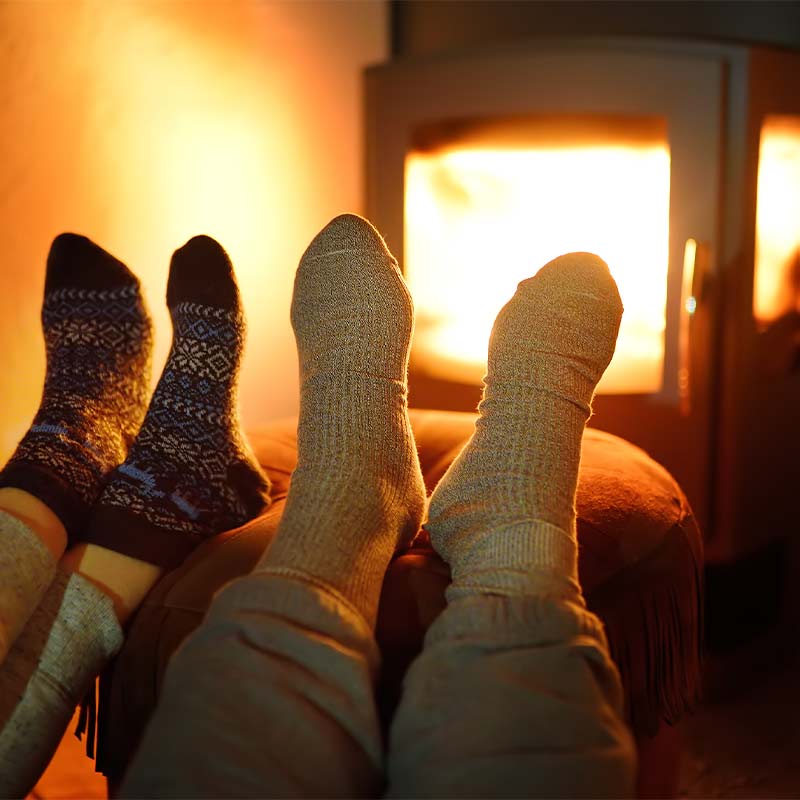 Kaksi paria kuviollisia ja vaaleita villasukkia lämpimässä oranssinkajoisessa takkatulessa.