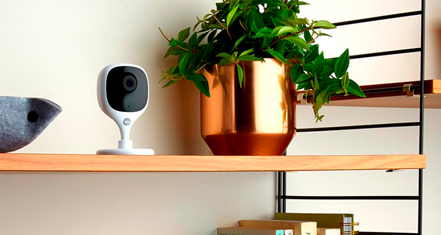 Valkoinen älykamera puisella hyllyllä, kuparinen ruukku ja roikkuva vihreä kasvi