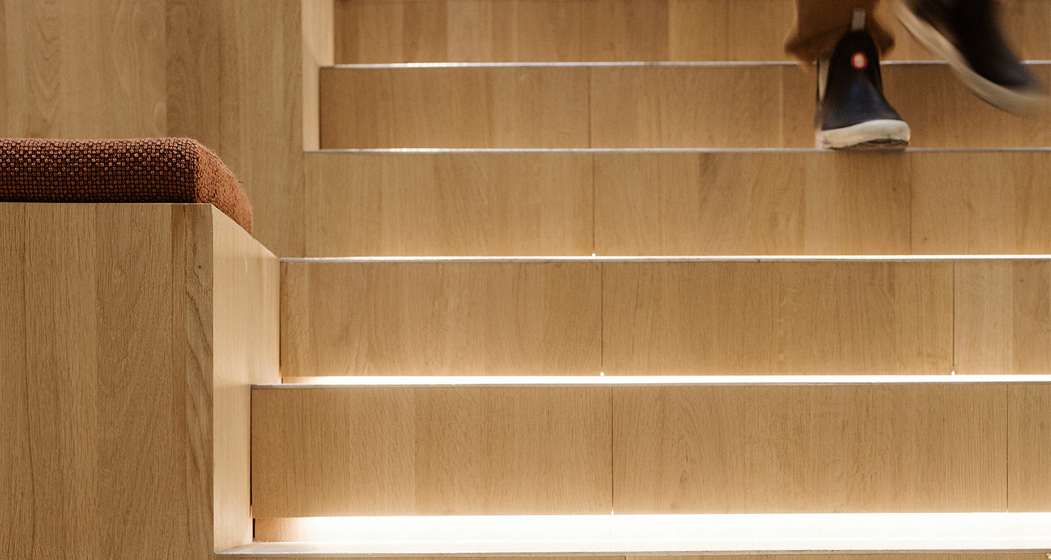 Vaaleat puuportaat integroidulla LED-valolla, punertava istuintyyny vasemmalla ja jalka yläkulmassa.