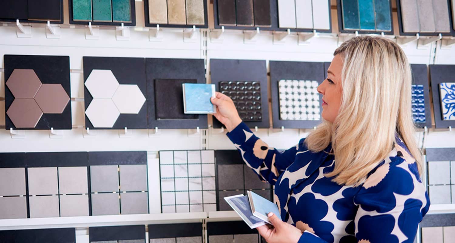 Nainen valitsee sinisiä ja harmaita laatanäytteitä telineeltä.