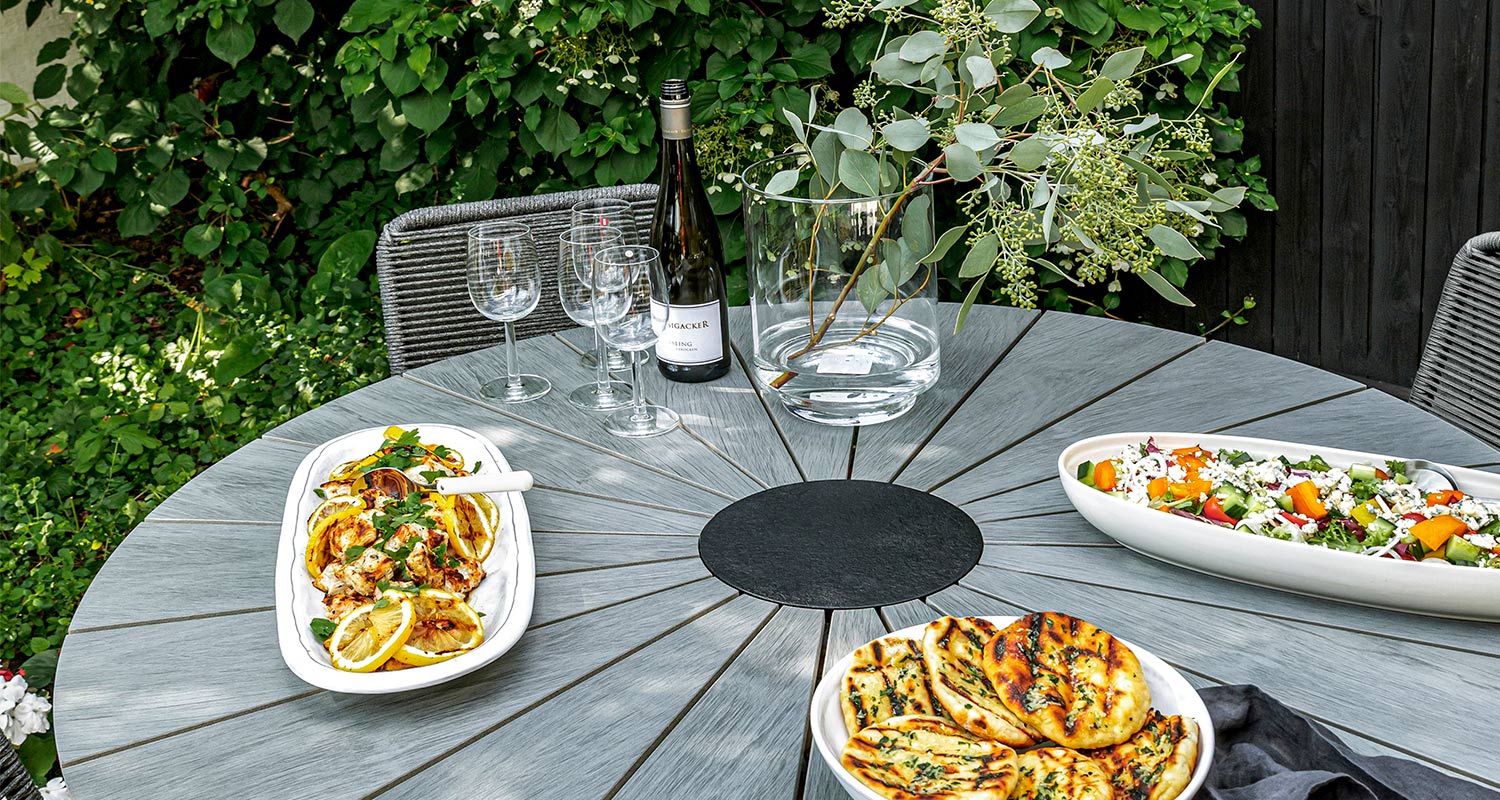 Harmaalta pyöreältä pöydältä eukalyptus, viinilasit, sitruunakanaa, salaatti ja grillileivät