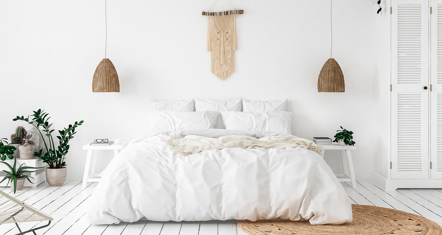 Valkoinen makuuhuone, valkoinen sänky, rottinkivalaisimet, viherkasvit, makrame ja juuttimatto.