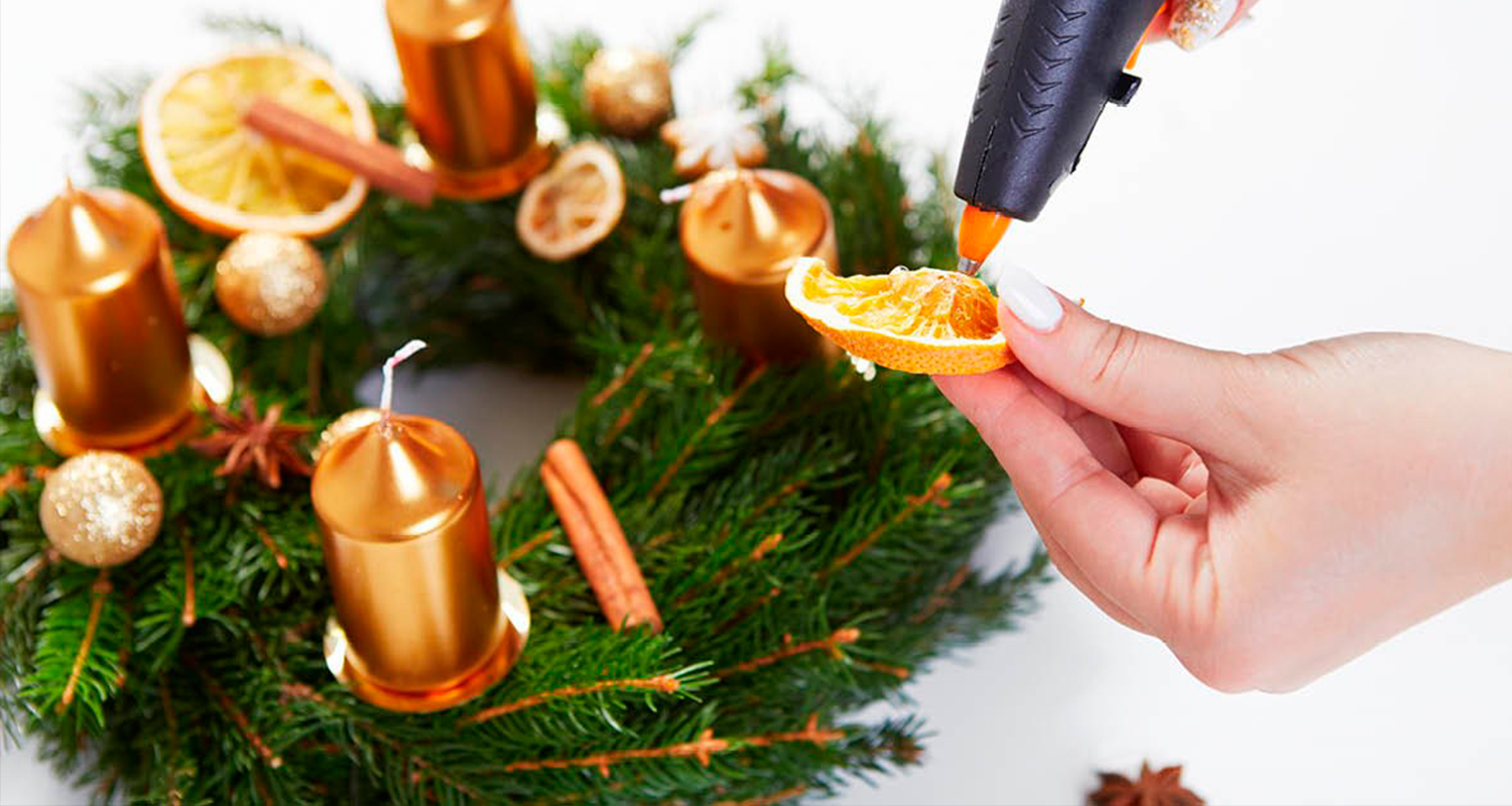 Joulukranssi saa koristeet, kun nainen koristelee joulukranssia ja käyttää liimapistoolia.