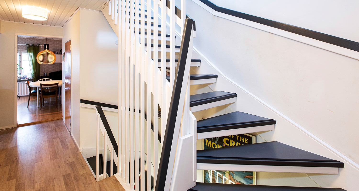 Valkoinen portaikko mustilla askelmilla eteisessä, takana ruokailutila vihrein verhoin.