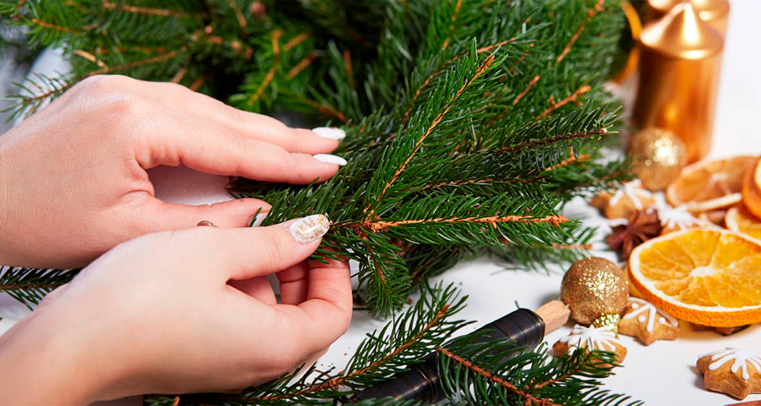 Nainen solmii yhteen havuja, kun hän tekee kaunista joulukranssia. Joulukranssi on valmistettu K-Raudan ohjeilla.