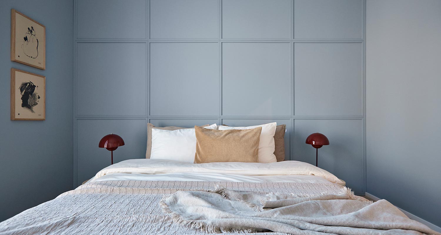 Makuuhuoneessa vaaleansininen paneeliseinä, valkobeige sänky, punaiset lamput, mustavalkoiset taulut.