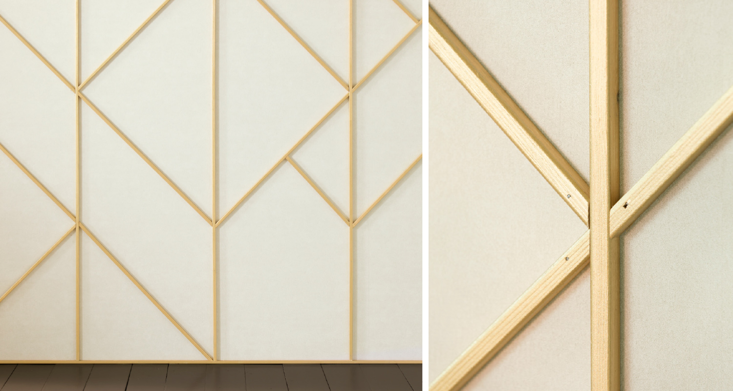 Vaalea paneeliseinä ohuilla vaalean puun geometrisillä listoilla ja tumma lattianraja.