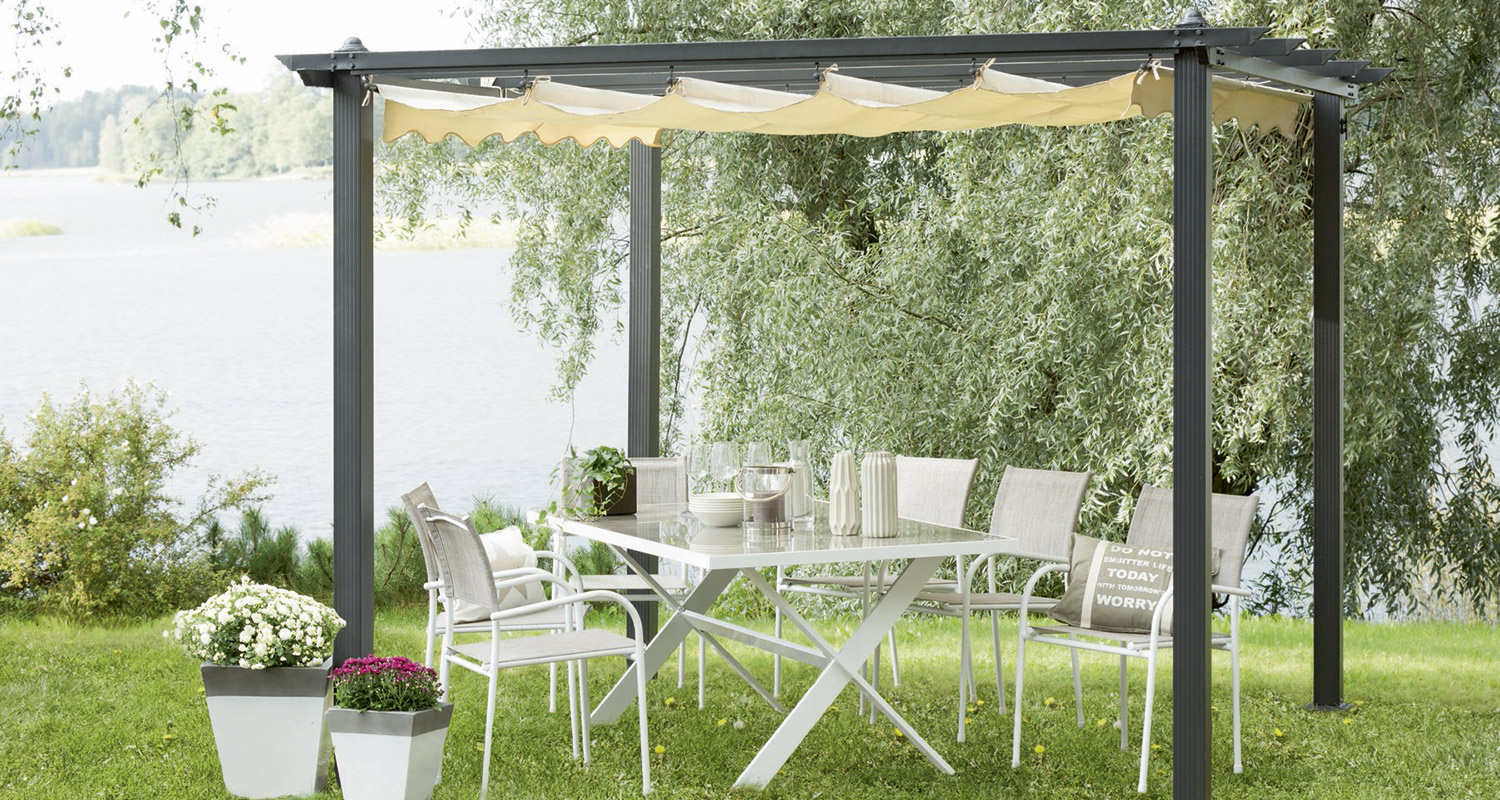 Valkoinen metallipöytä ja tuolit vaalean katoksen alla järven rannalla, ruukkukukkia