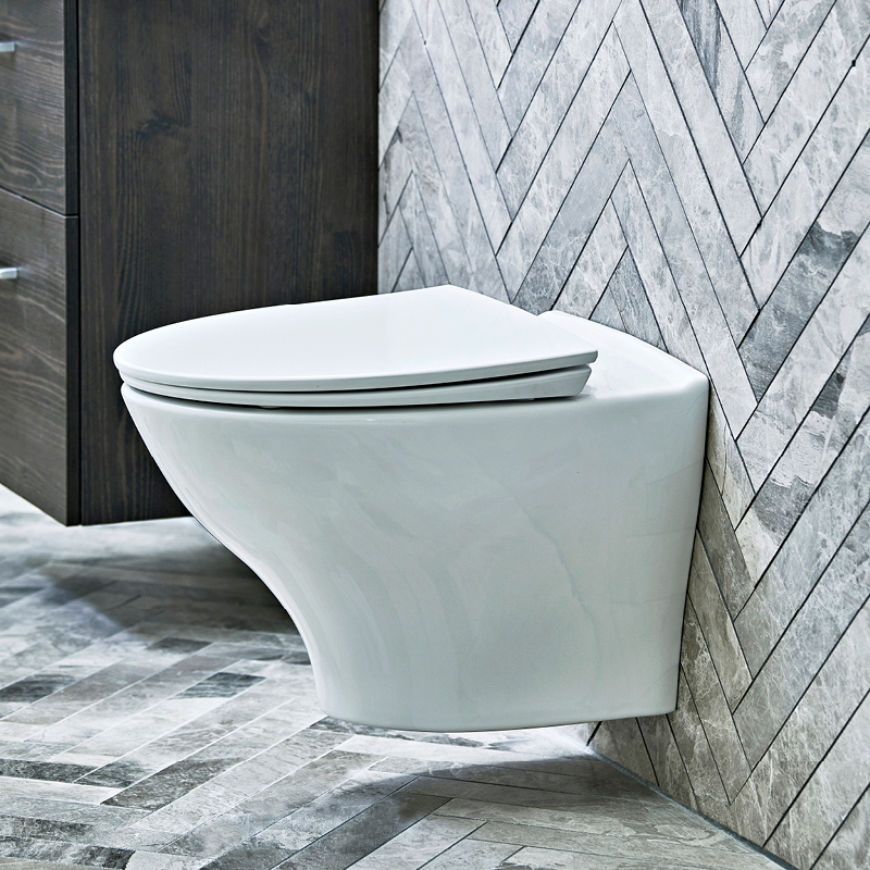 Seinään kiinnitetty valkoinen wc-istuin harmaalla kalanruotoladotulla laatta­­taustalla.