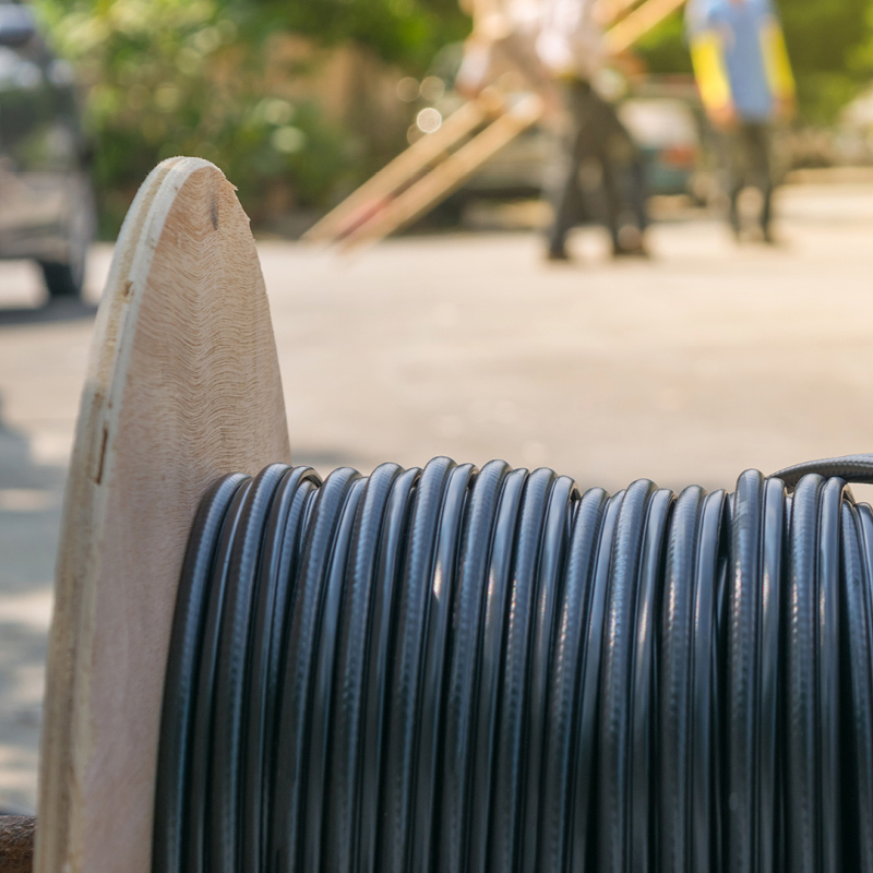 Puinen kelarulla mustaa kaapelia katutöiden reunassa, taustalla työntekijöitä.