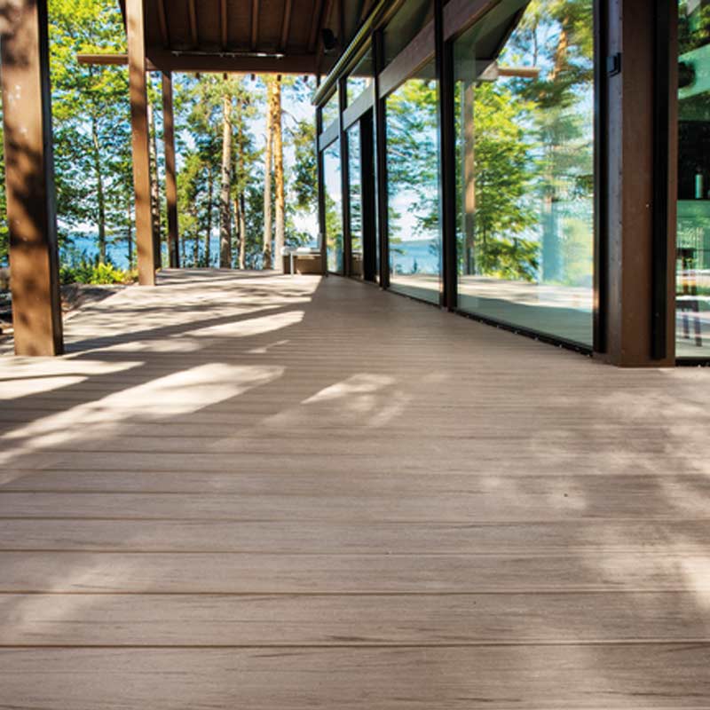 Moderni lasiseinäinen terassi järven rannalla, puupilarit, metsän vihreät varjot.