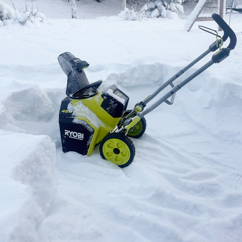 Akkulumilinko Ryobi RY18STX45A-240 18V ONE+ auratun alueen keskellä lumisessa pihassa, tuote on myynnissä K‑Raudassa.