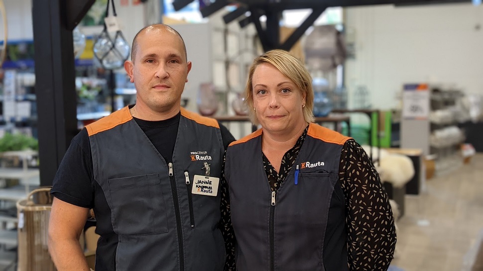 Kaksi K-Rauta-liivissä olevaa myyjää rautakaupan sisällä, hyllyjä ja työvälineitä taustalla.