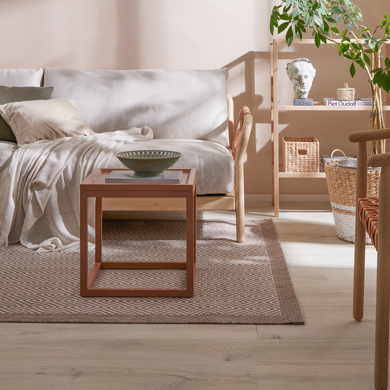 Olohuoneessa beige seinä, vaalea sohva, punaruskea pöytä, vihreä kulho, korikorit ja viherkasvi