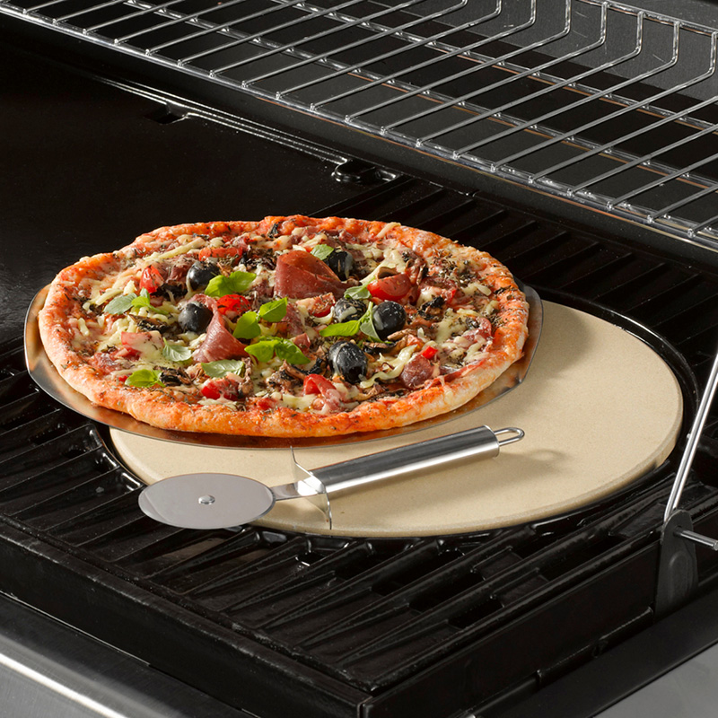 Pizzakivellä uunissa rapea pizza tomaatilla, mustilla oliiveilla, basilikalla ja pizzaleikkuri.